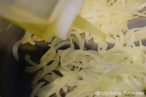Olive oil being squirted on sliced onions in a pan.