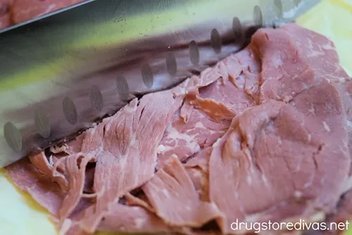 Deli slices of corn beef being cut with a knife.