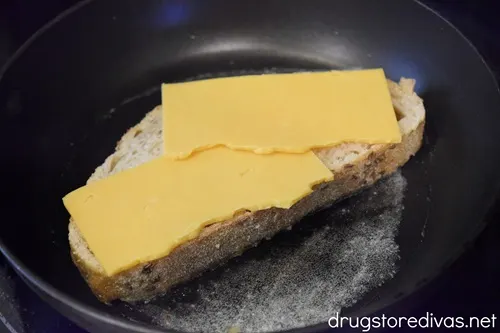 A slice of rye bread with cheese on it on top of melted butter in a pan.