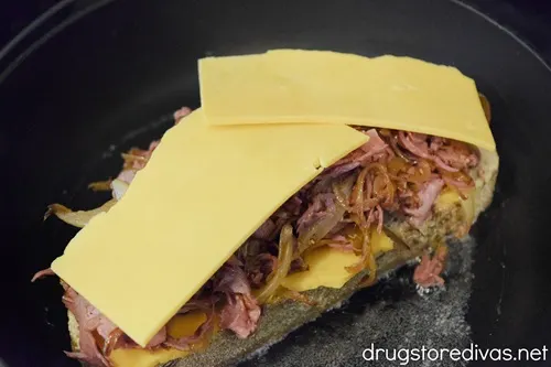 A slice of rye bread with cheese and sliced corned beef with onions on it on top of melted butter in a pan.