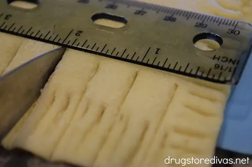 A ruler measuring puff pastry that's being cut by a knife.