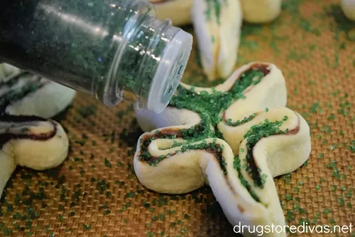Green sprinkles being sprinkled on top of shamrock shaped puff pastry.