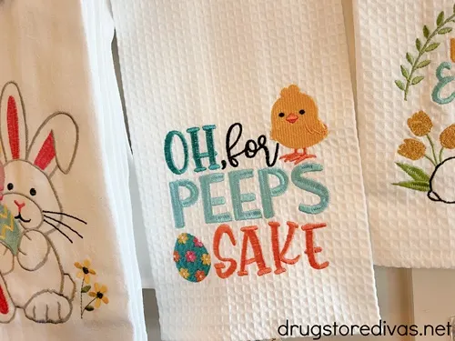 A white kitchen towel that has a small chick and Easter egg on it and says, "Oh, for Peeps Sake" on it.