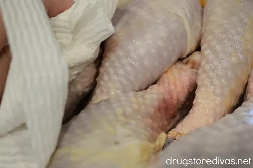 Chicken drumsticks being dried with a paper towel.