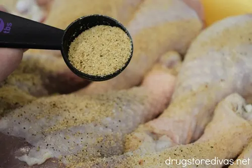 Spices in a measuring spoon above chicken drumsticks.