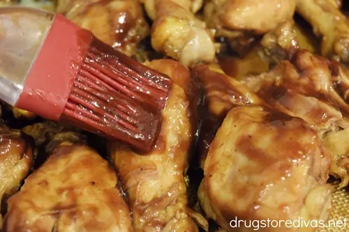 A pastry brush brushing sauce on chicken drumsticks.