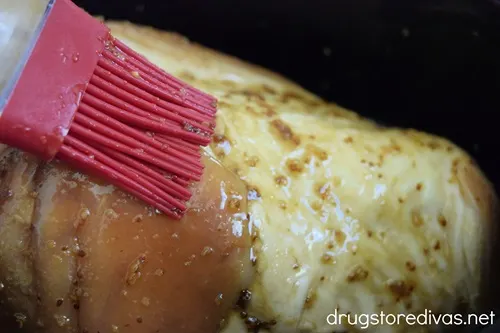 A red pastry brush putting glaze on a ham.