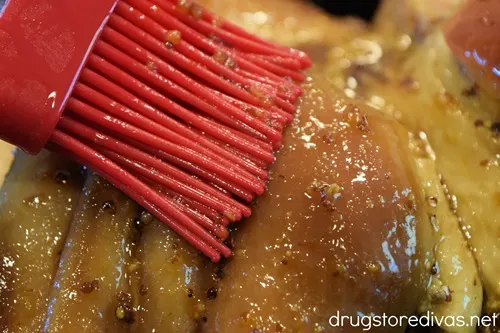 A red pastry brush putting glaze on a ham.
