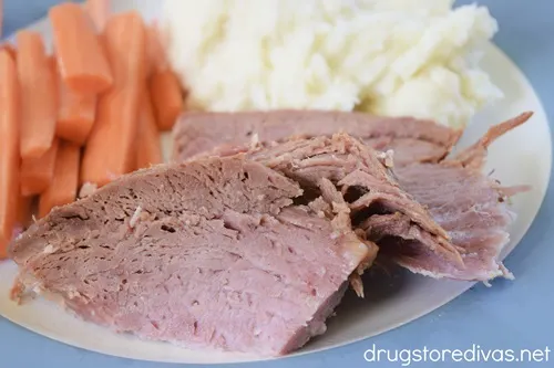Slices of ham on a blue and white plate with carrots and mashed potatoes,