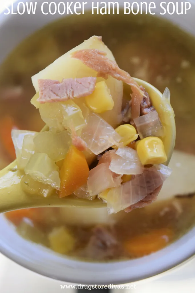 A yellow spoon with onion, potatoes, celery, carrots, corn, and ham in it and the words "Slow Cooker Ham Bone Soup" digitally written on top.