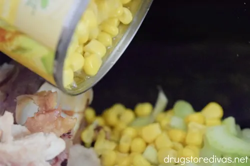 A can of corn being poured on top of chopped vegetables in a slow cooker.