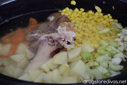 Chopped carrots, celery, and potatoes, plus a ham bone and chicken broth in a slow cooker.