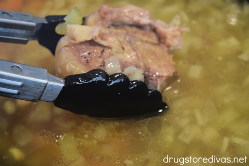 Tongs removing a ham bone from slow cooker soup.