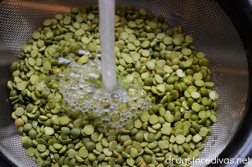 Dried peas in a colander being rinsed by water.