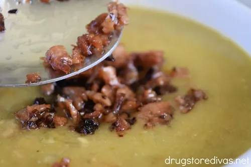 Crispy ham pieces on a spoon being put onto a bowl of split pea soup.