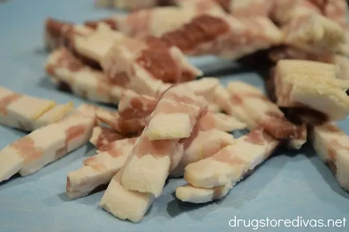 Chopped raw bacon on a blue cutting board.
