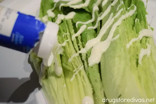 Salad dressing being poured on cut romaine lettuce halves.