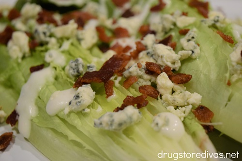 Bacon pieces and bleu cheese crumbles and white salad dressing on romaine lettuce halves.