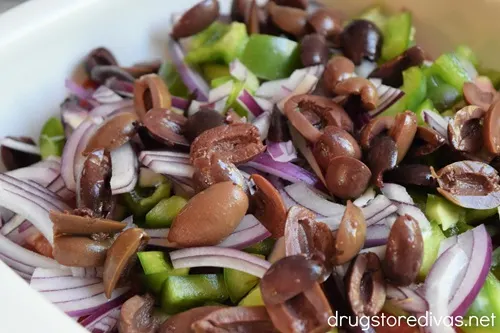 Cucumber, olives, red onion, green pepper, and tomato pieces in a white bowl.