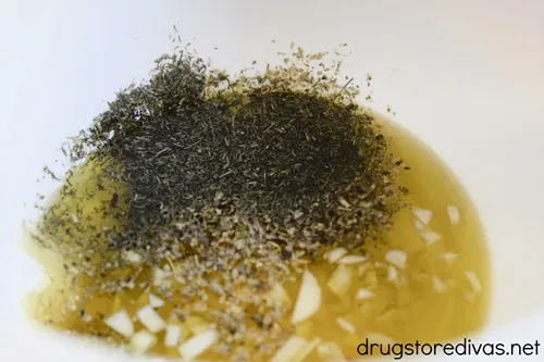 Olive oil in a white bowl with chopped garlic and herbs.