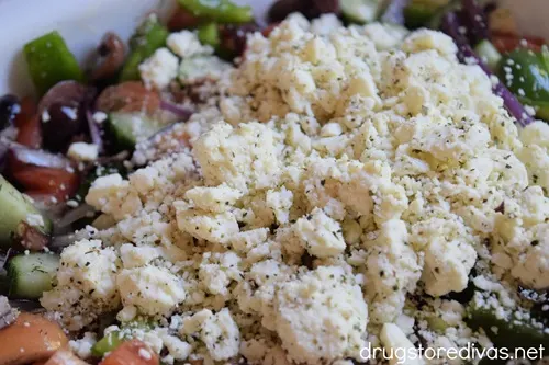 Feta cheese on top of a Greek salad in a white bowl.
