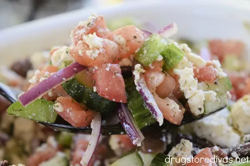 A spoon filled with Horiatiki, a Classic Greek Salad, over a white bowl filled with the salad.