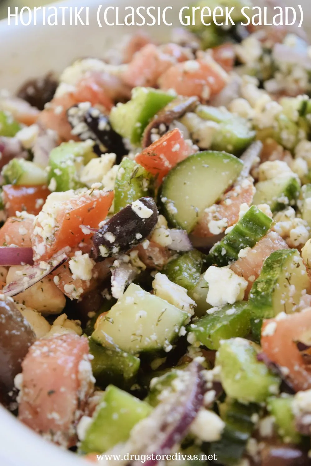 A white bowl filled with cucumbers, sliced olives, tomato pieces, sliced red onions, and feta cheese with the words 