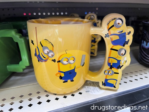 A yellow mug with Minions on the front and the handle on a shelf at a store.