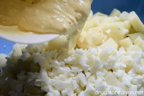 A yellow dressing being poured onto chopped egg whites and diced potatoes.