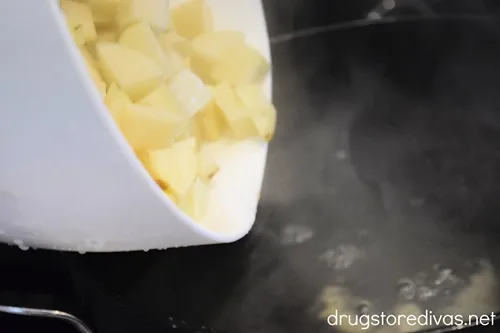 Diced potatoes in a white bowl being poured into a pot of water.