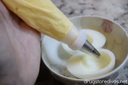 A yolk mixture in a piping bag being piped into two egg white halves.