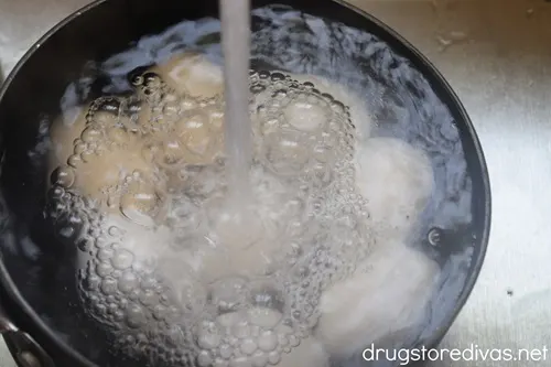 Cold water running over eggs in a pot.