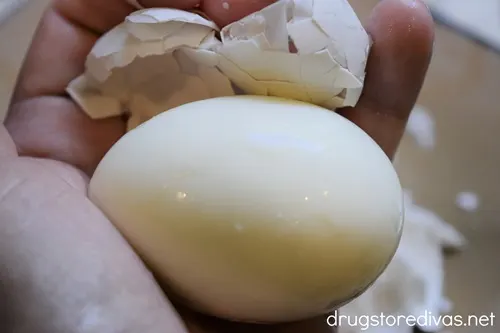 A hand holding a peeled egg with the shell above it.