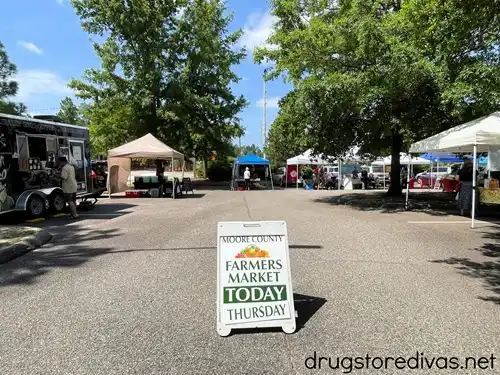 A sign advertising the Moore County Farmers Market in Southern Pines, NC with vendor tents around it.