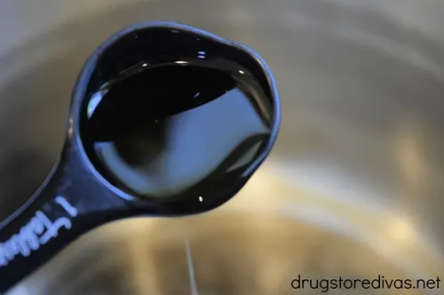 Liquid in a measuring spoon being poured into a metal pot.