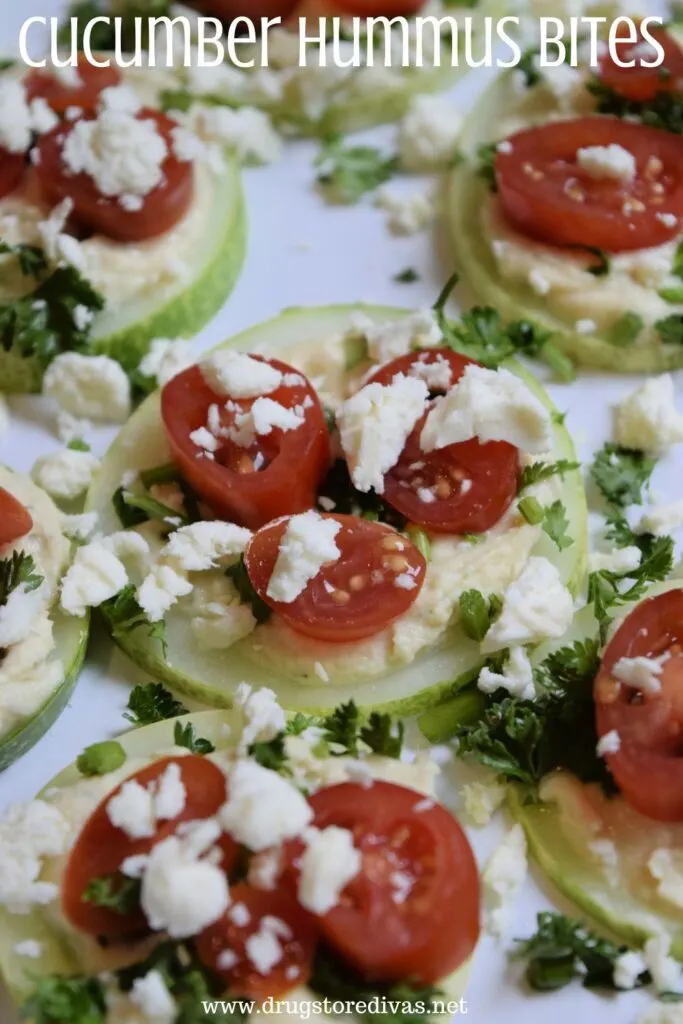 Slices of cucumber with feta, fresh herbs, and small tomato slices on top with the words "Cucumber Hummus Bites" digitally written above them.