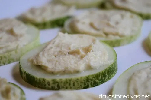 Hummus on top of cucumber slices on a white serving tray.