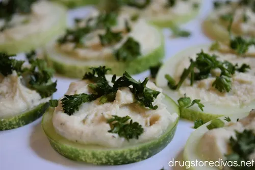 Chopped parsley and hummus on top of cucumber slices on a white serving tray.