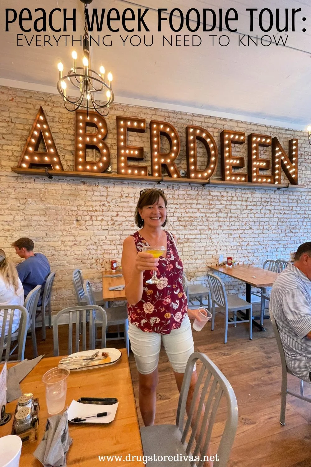 A woman holding a cocktail in a restaurant with the word ABERDEEN in lights above her with the words 