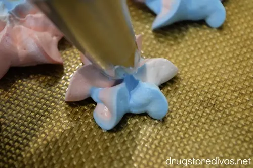 Red, white, and blue meringue cookies being piped onto a silicone baking mat.