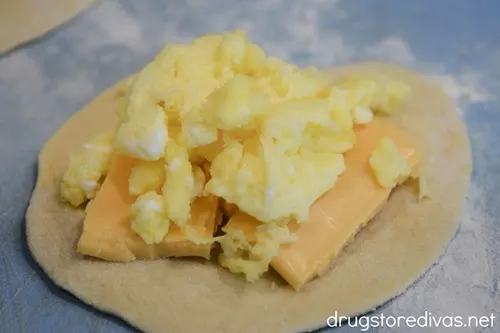 Four chunks of cheese and scrambled eggs on a rolled out biscuit.