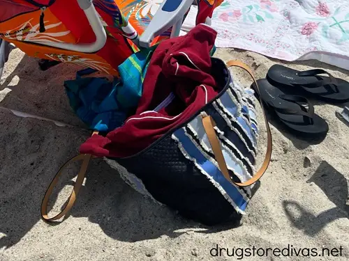 A beach bag on the sand at the beach next to a beach chair.