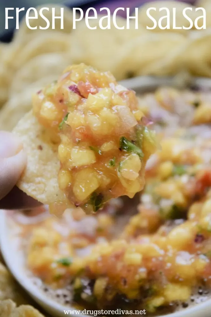 Fingers grabbing a round tortilla chip with fresh salsa on it over a bowl of chips and salsa with the words "Fresh Peach Salsa" digitally written on top.
