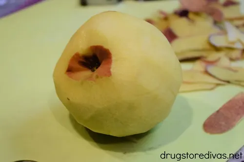 A peeled peach on a cutting board with the peeled skin behind it.