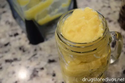 A mason jar filled with frozen peach lemonade and a blender behind it.