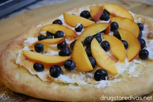 Pizza crust with goat cheese, blueberries, and peach slices on top.
