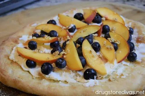 Pizza crust with goat cheese, blueberries, peach slices, and granola on top.
