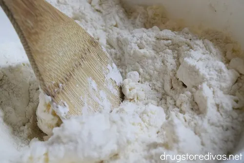 A bamboo spoon stirring white cake mix in a bowl.