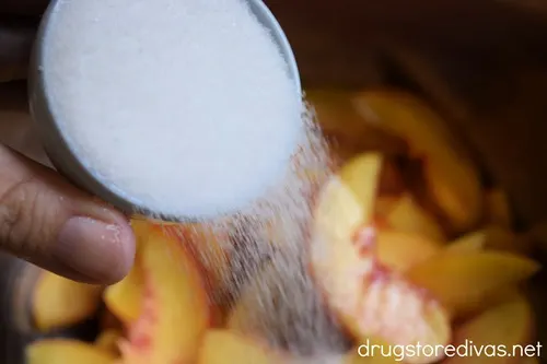 Sugar in a measuring cup being poured on peach slices.