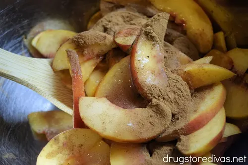 Peach slices with cinnamon on top being stirred by a bamboo spoon.